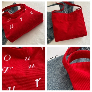Detail view of red corduroy tote bag showing white letter embroidery and wide shoulder strap