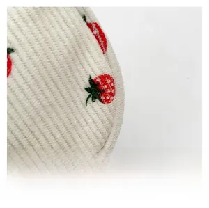 Détail du velours côtelé crème avec broderie de fraises rouges et coutures précises