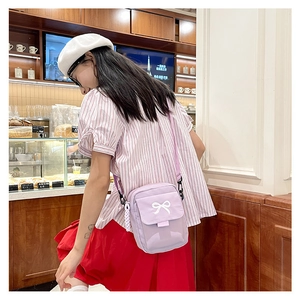 Detail of a purple canvas crossbody bag with a white bow decoration on a model
