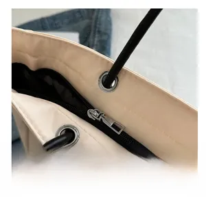 Detailed close-up of smooth silver zipper and rope handle on cream tote bag
