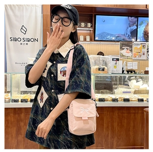 Detail of pink canvas crossbody bag with white bow embroidery in a warm cafe setting