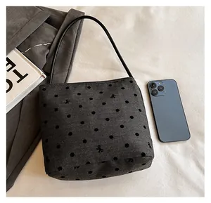 Detail showing the polka dot canvas texture and embroidered bow on the dark gray tote bag
