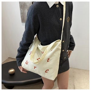 Close-up of cream corduroy tote bag featuring red embroidered letters and ribbed texture