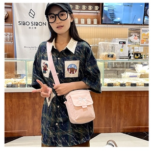 Detailed view of pink canvas crossbody bag with white bow embroidery on a female model