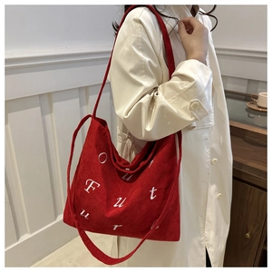 Detail of red corduroy tote bag featuring white embroidered letters and textured fabric
