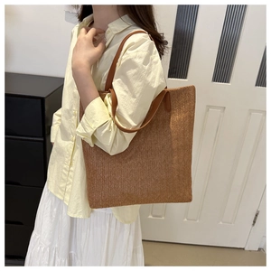 Détail d'un sac cabas en paille tissée marron avec des bandoulières en cuir résistantes