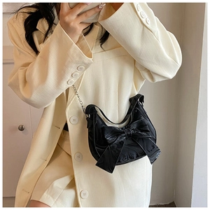 Detail of black glossy patent leather hobo bag with oversized bow and silver chain strap