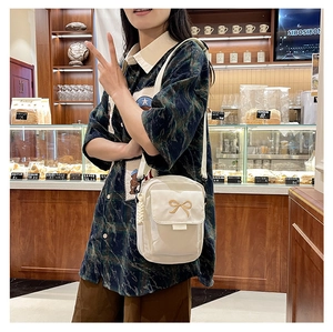 Close-up of golden bow embroidery and front pocket on a beige canvas crossbody bag