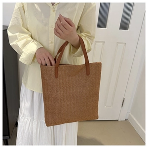Détail d'un sac cabas en paille tressée avec anses en cuir marron porté par un mannequin