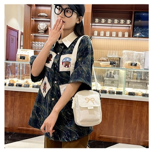 Detailed view of white crossbody canvas bag with gold bow embroidery and thick rope zipper pull