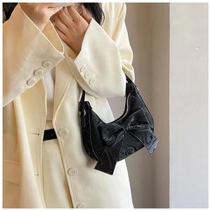Detail of black glossy bow shoulder bag shown with chic cream outfit for women