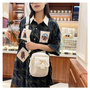 Detail of white canvas crossbody bag with delicate gold bow embroidery and woven zipper