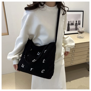 Detail of black corduroy tote bag with culture embroidery worn on shoulder in a home setting