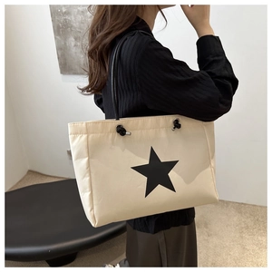Detailed view of spacious beige tote bag with black star motif and rope straps