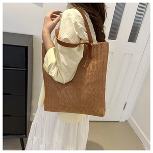 Détail d'un sac cabas en paille tissée avec anses en cuir marron porté par un mannequin