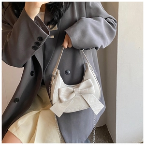 Chic beige handbag featuring a large decorative bow and elegant silver chain strap detail