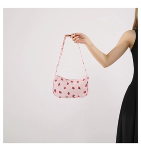 Sac sous le bras en velours rose avec imprimé fraise porté par un mannequin sur fond clair