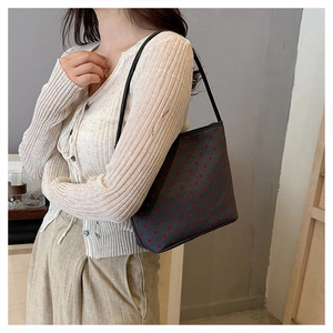 Detail view of a gray underarm bag with red heart patterns and black leather strap