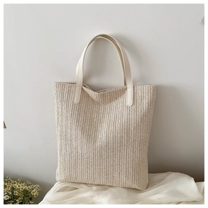 Détail d'un cabas tressé beige avec anses en cuir blanc sur fond de satin blanc