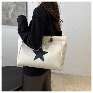 Detailed side view of a large beige tote bag with black star print and slim shoulder straps