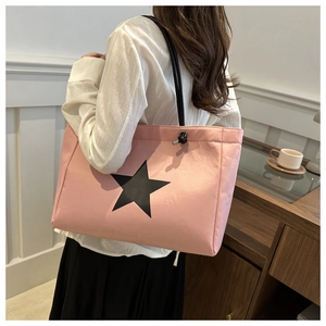 Detail of pink tote bag with black star pattern shown on a shoulder in indoor scene