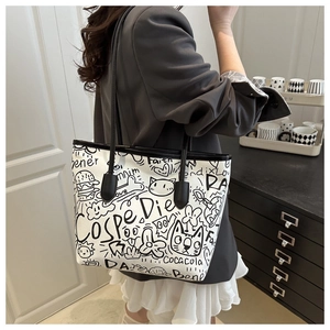 Detailed view of large canvas tote bag featuring black and white graffiti and leather straps