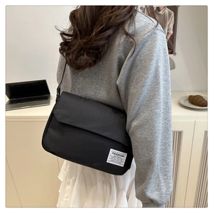 Close-up of black Oxford cloth messenger bag with flap closure and woven brand tag