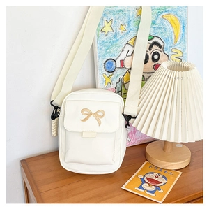 Close-up of white canvas shoulder bag featuring brown embroidered bow and strap detail