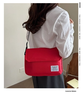 Close-up of red Oxford cloth crossbody bag featuring a white woven label and adjustable strap