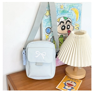 Detail of light blue crossbody bag with bow embroidery and woven charm on a table
