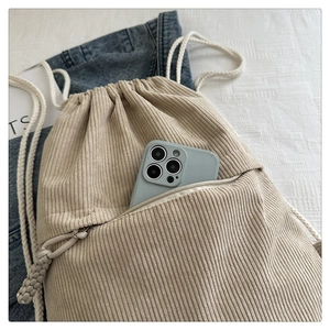 Detail of beige corduroy drawstring backpack showing the front zipper pocket and texture