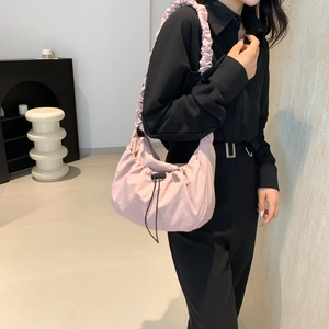 Minimalist light pink drawstring nylon tote bag worn by a model in casual black outfit