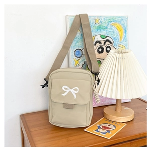 Close-up of beige canvas crossbody bag featuring bow embroidery and woven rope charm
