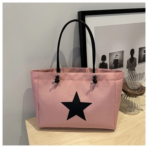 Detailed shot of pink tote bag with black star motif and thin leather straps on a wooden table