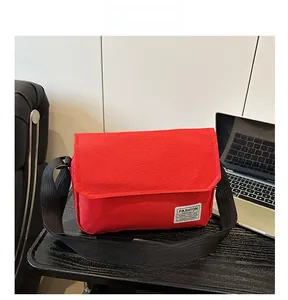 Detail of red oxford messenger bag with adjustable strap and brand logo on the corner