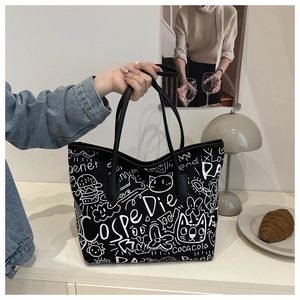 Detailed view of the black canvas tote bag featuring white graffiti prints and leather straps