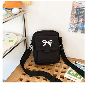 Detail view of black crossbody bag with white bow embroidery and woven strap on wood