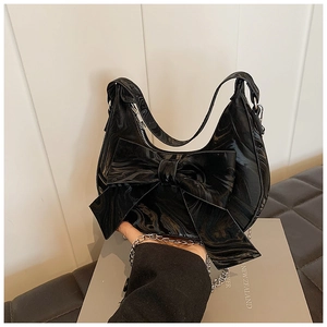 Detail of glossy black marble-textured patent leather bag with a large bow and silver chain
