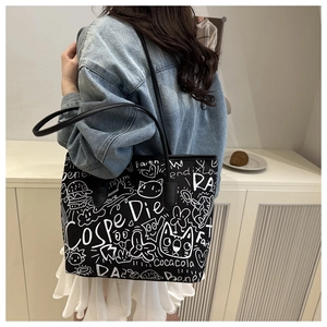 Detailed side view of black canvas tote bag with white graffiti patterns worn by a model