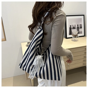 Detalle del bolso tote de lona a rayas azules con lazo de encaje blanco y correa de hombro