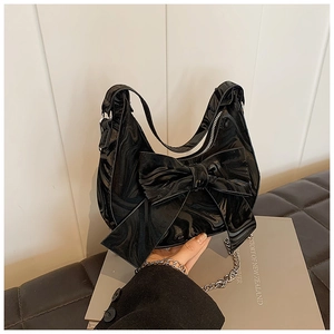 Detail of black glossy faux leather handbag featuring a large bow and silver chain strap