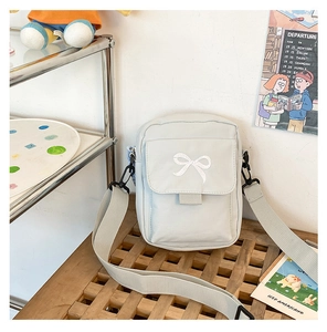 Detail of light gray canvas crossbody bag featuring delicate white bow embroidery
