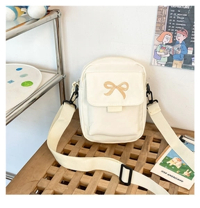 Detail of a beige canvas crossbody bag with a brown bow embroidery and adjustable black strap