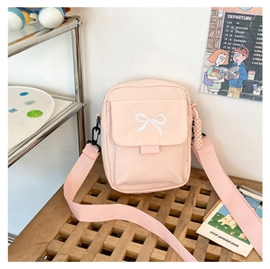 Close-up of pink crossbody bag featuring white bow embroidery and front flap pocket