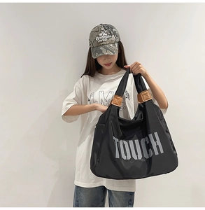 Dettaglio di una grande borsa tote in nylon nero con stampa TOUCH e manici in pelle marrone