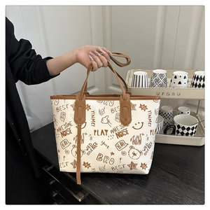 Detail of a beige tote bag featuring colorful cartoon graffiti prints and brown leather handles