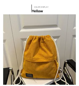 Detail view of yellow corduroy drawstring backpack with black Fashion label and white ropes
