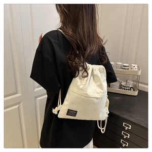 Close-up of white corduroy drawstring backpack showing the fashion label and texture