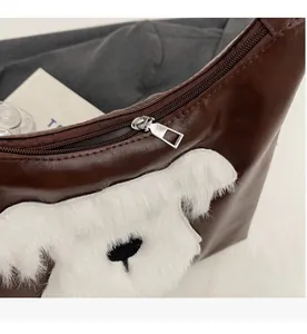 Détail de la fermeture éclair argentée et du patch en peluche sur le sac en cuir marron