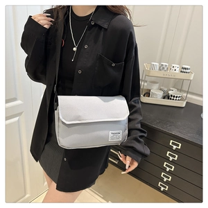 Gray oxford messenger bag with flip cover and fashion label shown on a side-profile model